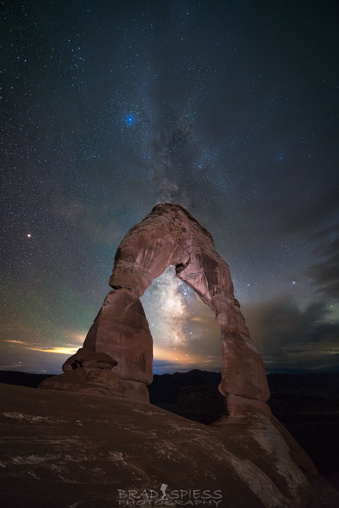 The Milky Way peaking its way out behind some clouds at Delicate Arch in Arches National Park.