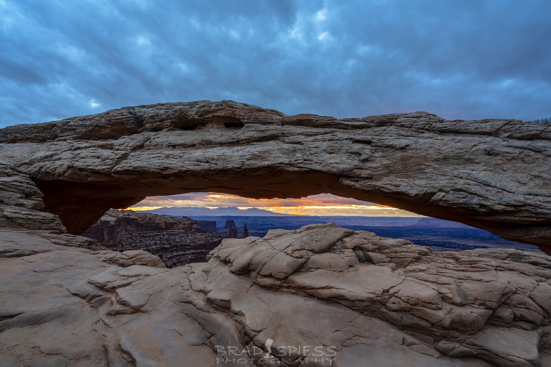 The sun lighting up the clouds in the distance seen through Mesa Arch