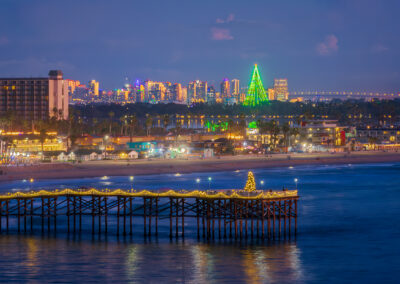 The holiday lights adorn Crystal Pier in Pacific Beach with a Christmas Tree at the end of the pier. In the background you can see the San Diego City Skyline along with the lights from the Coronado Bridge. To top it off the 320 foot tall Skytower at Sea World is decorated as Christmas Tree.